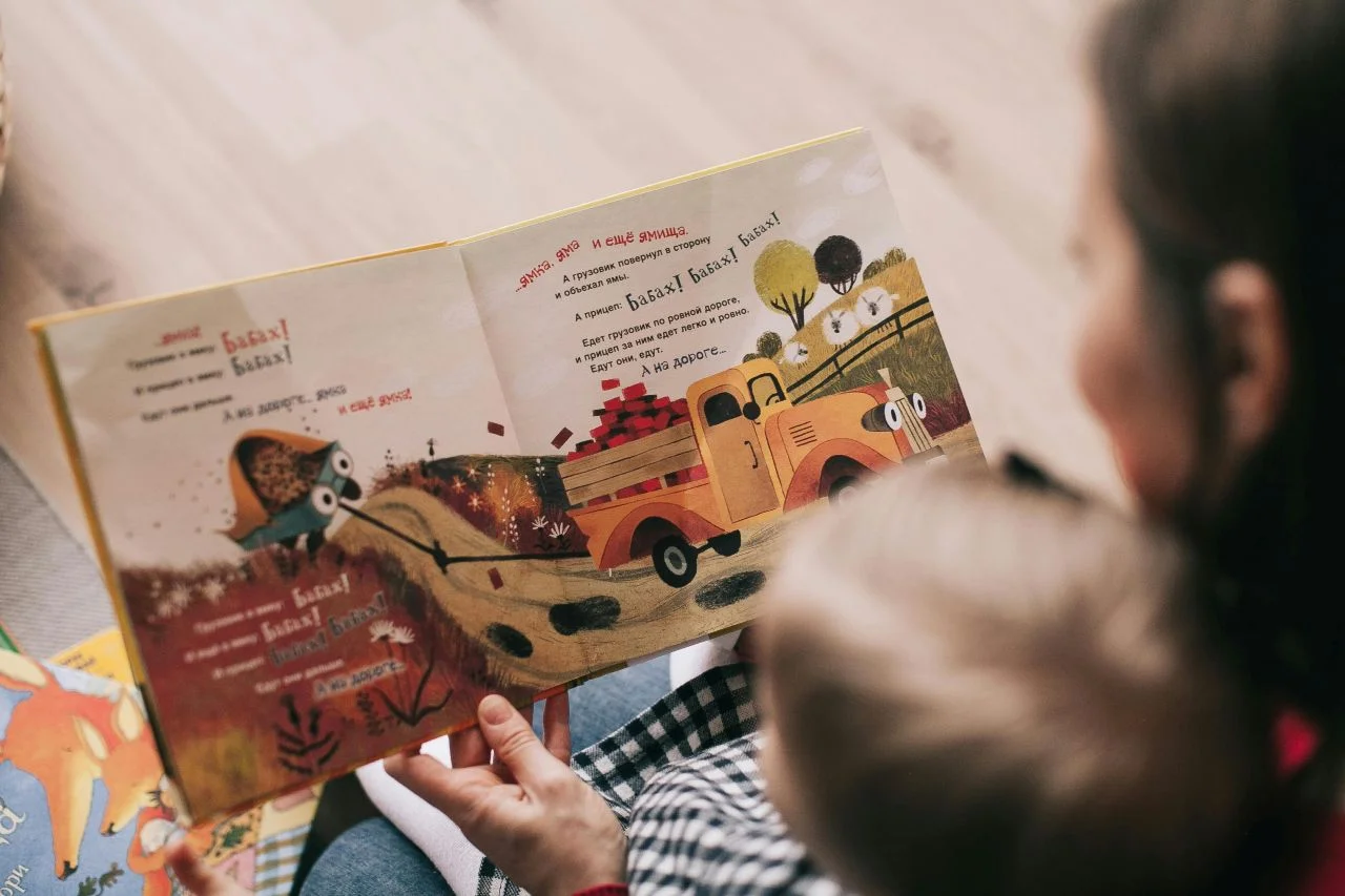 Elternteil liest einem Kind ein Bilderbuch über Familienvielfalt vor