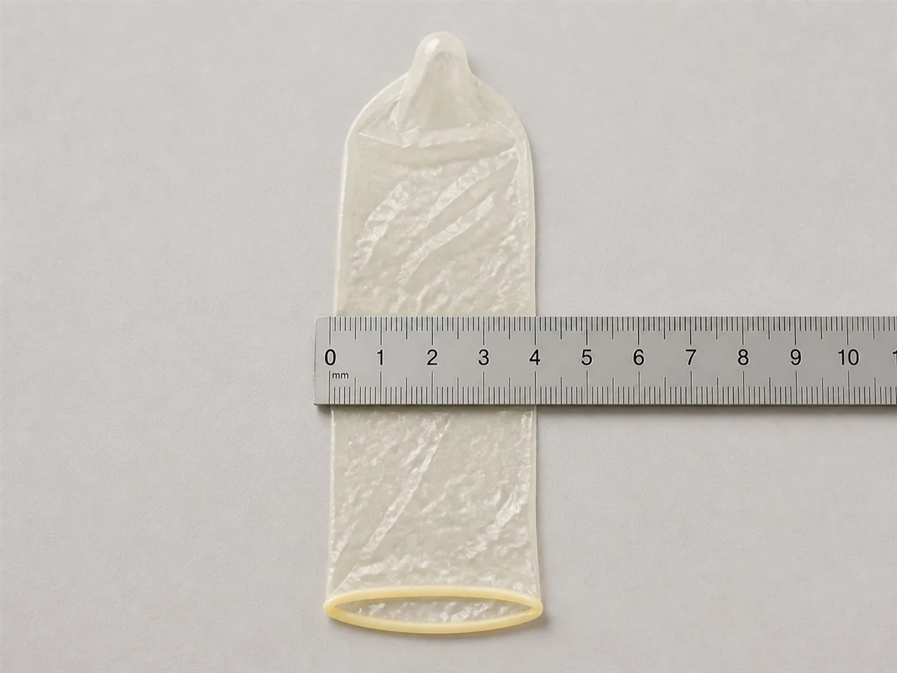 Kondom flach über ein Lineal gelegt, um die Breite in Millimetern sichtbar zu machen