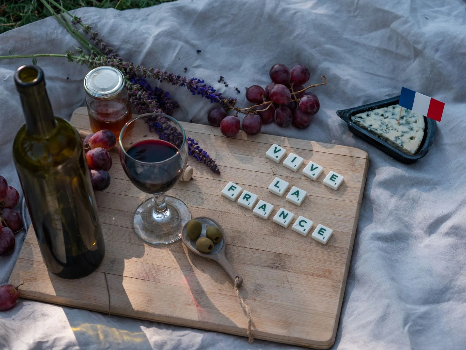 A French picnic with cheese, grapes, wine, a French flag and letter tiles arranged on a wooden board