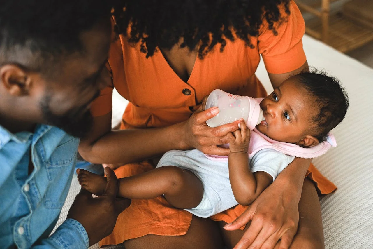 A baby is being held, with a breast pump and a baby bottle beside them as symbols of breastfeeding, expressing, and infant formula