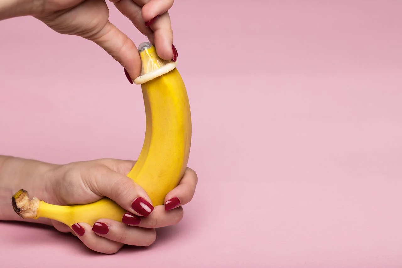 Hände demonstrieren an einem Bananenmodell, wie ein Kondom abgerollt wird