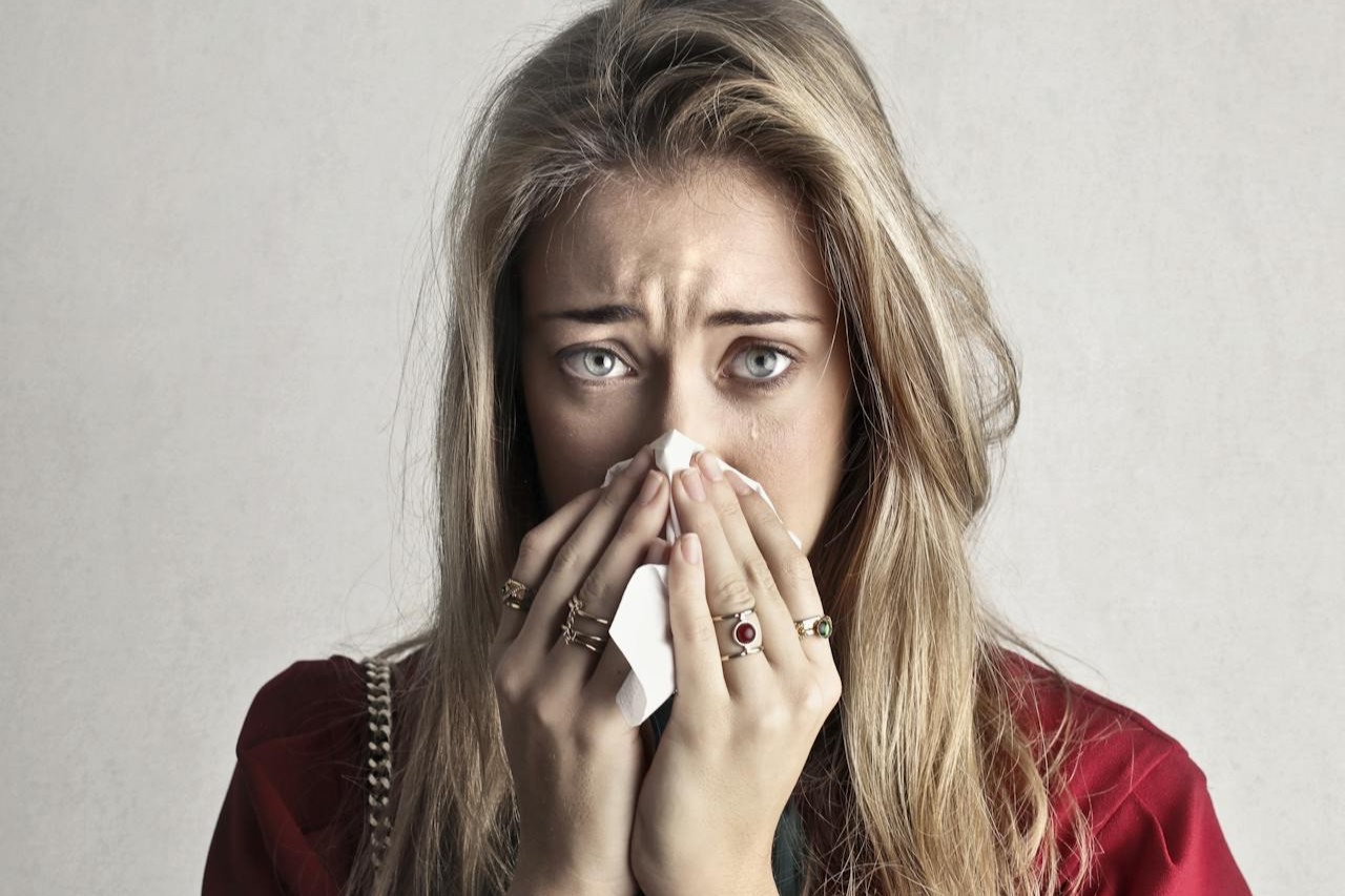 En gravid person sitter i soffan med te och näsdukar och mäter temperaturen för att bedöma förkylningssymtom